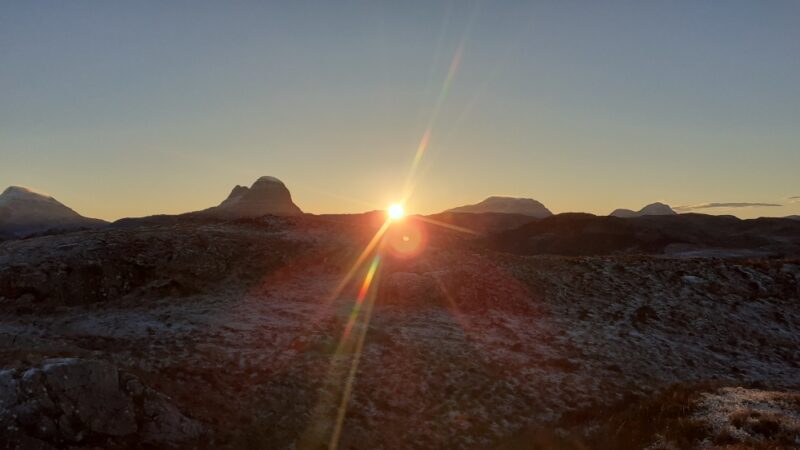 The blue silhouettes of Canisp, Suilven, Cul Mor and Cul Beg with the sun rising like a gold star on the high horizon between them
