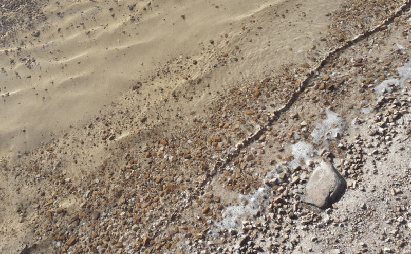 pale golden quartzite sand underlying shallow sunlit ripples, washing up on a creamy-pink quartzite pebbled loch shore