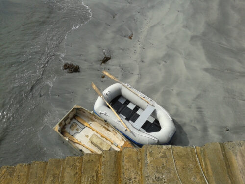 small scruffy fibreglass tender and inflatable grey tender beached side by side
