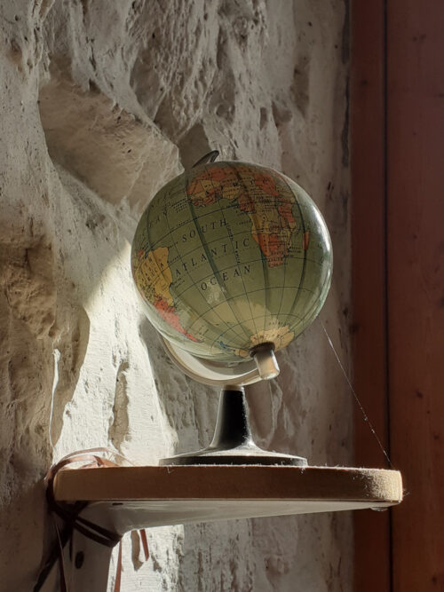 small globe on little shelf in a shaft of sunlight which illuminates a line of spider silk tethering the globe to the shelf